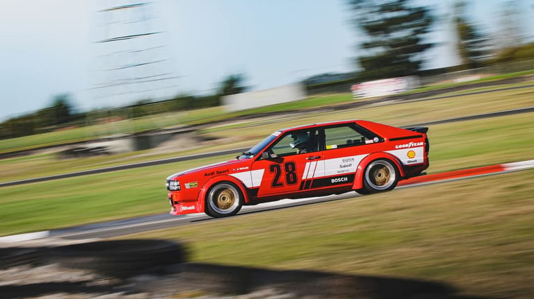 A vintage red Audi Sport Quattro race car speeding on a track with motion blur.