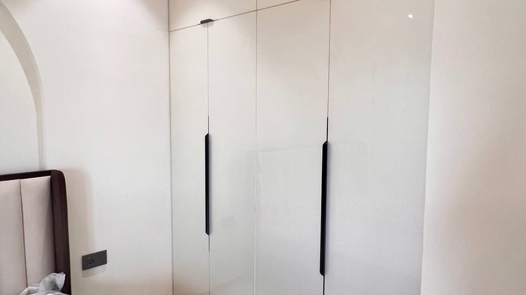 Modern white gloss fitted wardrobe with sleek black handles in a minimalist bedroom design.