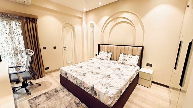 Modern bedroom with an upholstered queen bed, arched wall decor, and an office chair.