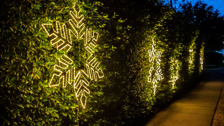 Illuminated snowflake Christmas decorations glow brightly on dark a hedge lining a HOA sidewalk