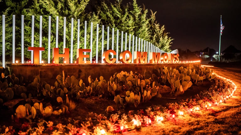Illuminated neighborhood entrance sign with festive holiday lights and desert landscaping at night.