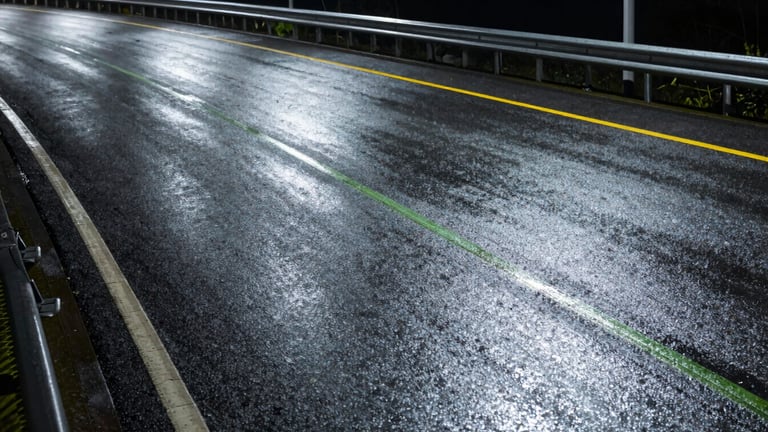 Wide panoramic shot of a dark highway curve at night, glowing yellow-green safety lines guiding the road edge under rainy conditions, high-contrast exposure.