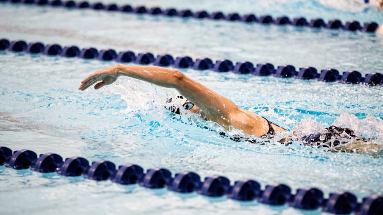 High-speed shutter shot of a swimmer's hand fending through crisp water, frozen droplets, deep navy lane lines, high contrast indoor pool lighting, 35mm