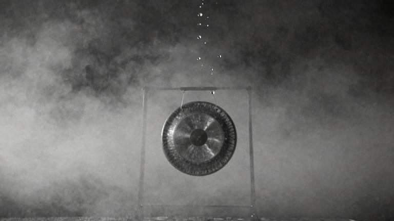 Surreal monochrome 35mm photography of water droplets suspended mid-air, floating upward towards a dark sky, a silent metal gong hovering in the misty background, high contrast ink-wash tones, ethereal diffused mist-light