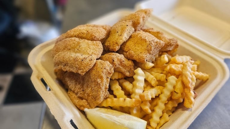Golden fried catfish and crinkle cut fries with a lemon wedge in a to-go container at Captain's Galley