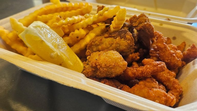 Fried oysters with fried clams, crinkle-cut fries and a lemon wedge in a takeout container from Captain’s Galley