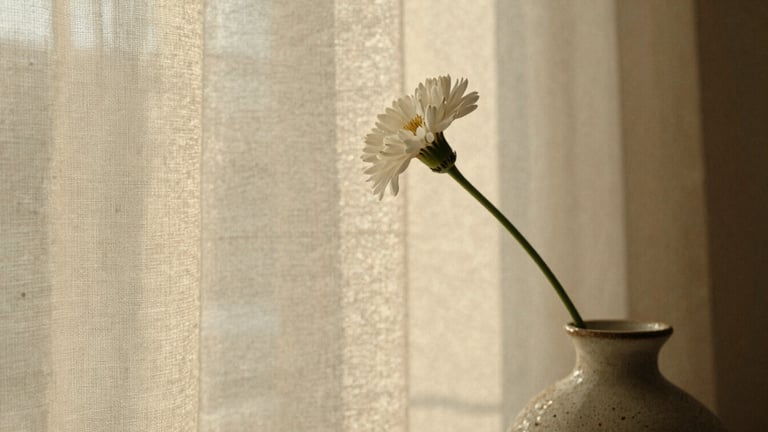 Close-up of raw linen texture, a single delicate white floral stem in a handmade ceramic vase, warm soft golden hour light, editorial 35mm film style.