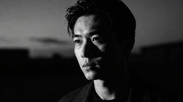 High-contrast portrait of the artist in shadow, deep twilight, 35mm anamorphic lens, cinematic film photography, dramatic chiaroscuro lighting.