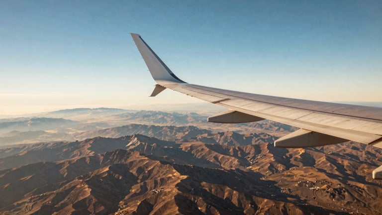 Wide panoramic view of an airplane wing over a vast alpine landscape, clear blue sky, crisp detail, warm editorial photography