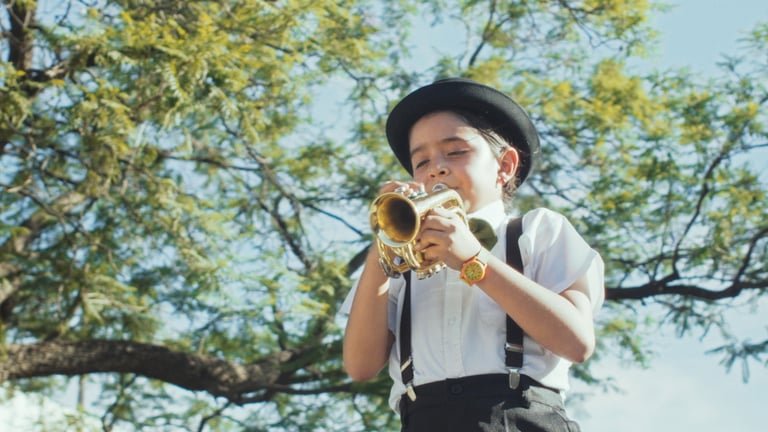 Una niña con sombrero y tirantes, tocando la trompeta.