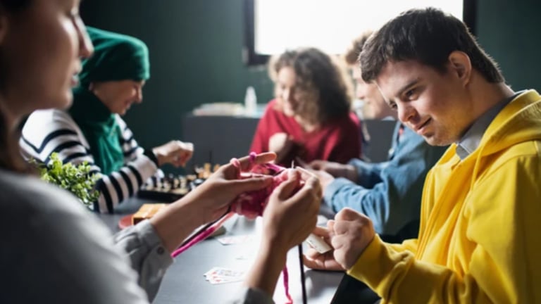 A group of people engaged in a social activity around a table, demonstrating NDIS community access