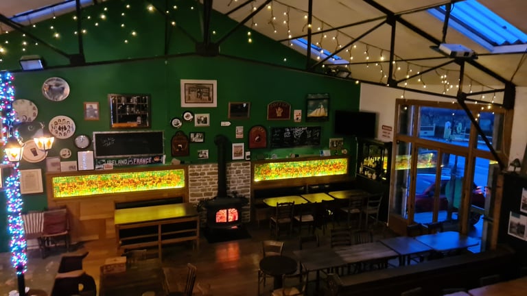 Cozy Irish pub interior with green walls, fairy lights, a wood-burning stove, and seating areas.