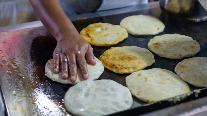 Hand-flattened pupusas cooking on a hot griddle, a traditional Salvadoran street food dish.