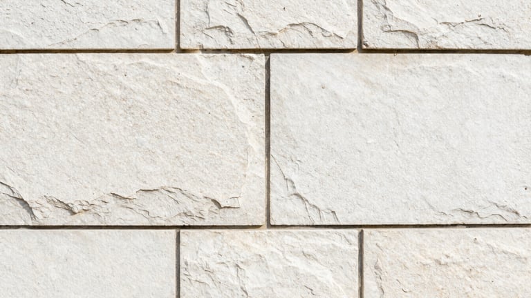 Tight macro detail shot of clean, precisely aligned stone blocks in a retaining wall, showing fine grout lines and texture, bright morning daylight, sharp focus.