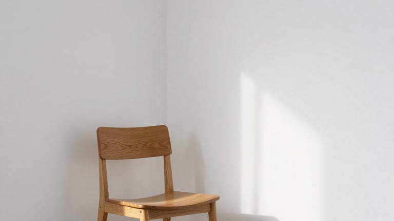 A serene corner of a minimalist studio, clean white walls, a single wooden chair, natural soft daylight casting gentle shadows, editorial atmosphere