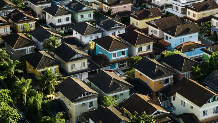 Aerial view of a dense suburban residential neighborhood with colorful modern houses and tropical trees.