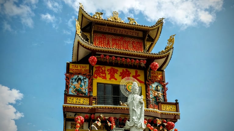 Exterior view of a vibrant yellow pagoda in Soc Trang, Vietnam with a white Guan Yin statue.