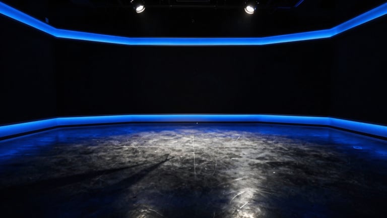A wide, cinematic empty broadcast studio at night, dramatic blue rim lights reflecting off polished concrete floors, high-contrast shadows, 35mm