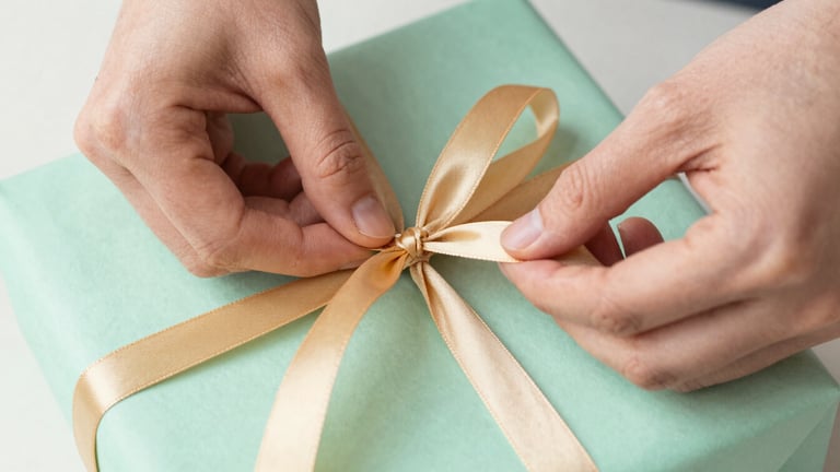 Close-up of hands carefully tying a warm gold ribbon around a mint green gift package, soft natural light