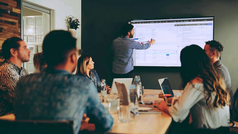 a team watches a colleague point at data on a large screen