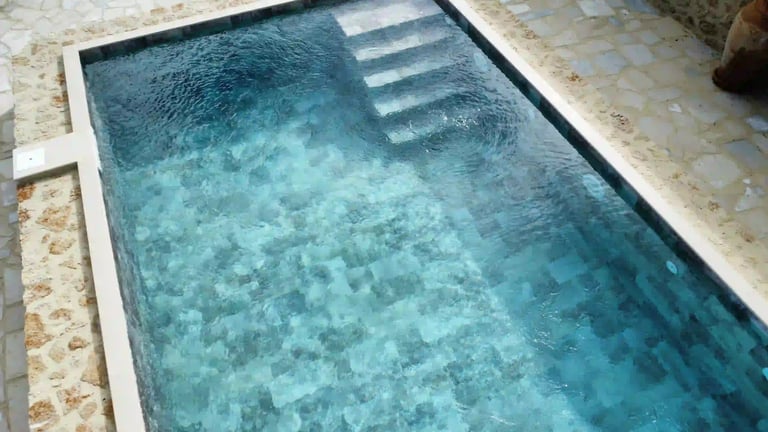 Overhead view of a modern backyard swimming pool with blue mosaic tile and stone patio.