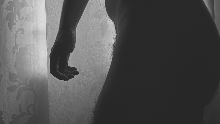 A silhouette of a buttock and a hand cast in shadow against a floral curtain.