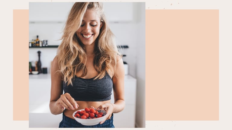 Smiling woman in fitness apparel holding a bowl of fresh raspberries and blueberries.