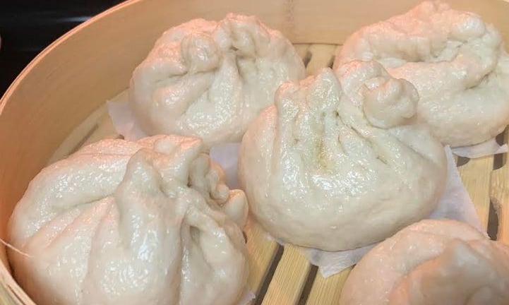 Steamed dumplings in bamboo steamer with steam rising. For FlavorfulBites