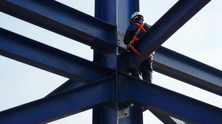 Detailed close-up of structural steel joints being bolted by a technician in full PPE, safety orange harness, high-contrast natural daylight, 35mm.