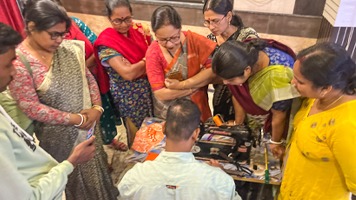 Eight women standing looking down at a sewing machine and fabric