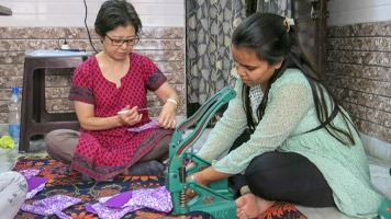 Two women using a snap machine to put snaps onto fabric sanitary napkins.