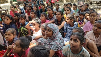 Large group of girls sitting on the ground listening to a talk.
