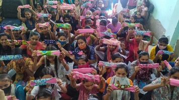 Thirty girls in a small classroom holding up Hanaru's sanitary napkins.