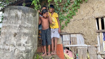  boys standing by cement water tank beside traditional West Bengal house.