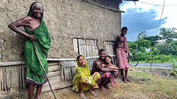 4 people in traditional dress outside traditional West Bengal home.