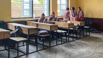 Classroom with long bench desks and a few girls.