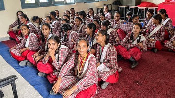 Around 30 girls in uniform sitting on floor in classroom.