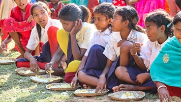 6 girls sitting on grass eating from plates of food on grass.