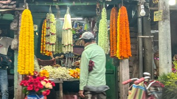 Man outside stall selling flower malas, used for ritual. Yellow cream and orange flowers.