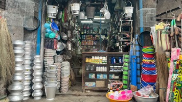 Tiny Indian shop crammed with saucepans and buckets and other household items for sale.