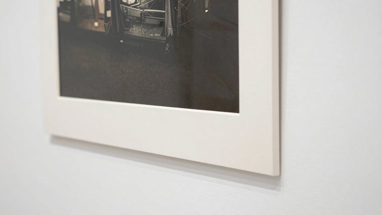 Close-up detail of the edge of a large-format archival pigment print, showing the paper texture and mounting on acid-free dibond, clean white background, soft diffused light, straight-on framing.