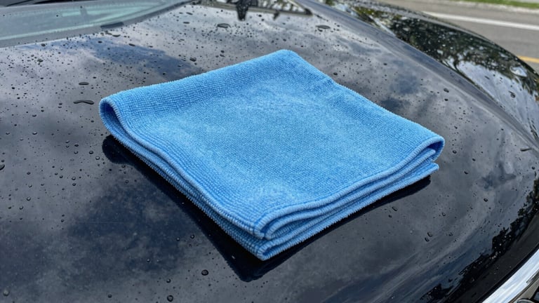 Close-up of water beautifully beading on a freshly waxed deep black car hood, electric baby blue microfiber cloth wiping the surface, high-contrast reflections.