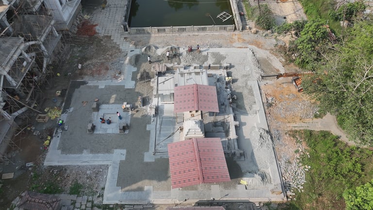 Aerial view of a traditional Hindu temple under construction with red roof panels and stone masonry.