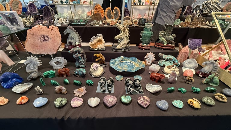 A collection of colorful polished gemstones and crystal animal carvings displayed on a table at a gem show.