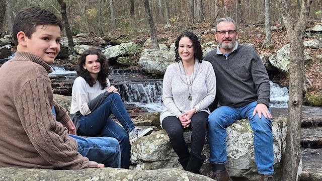 a family sitting on a rock formation in a wooded area