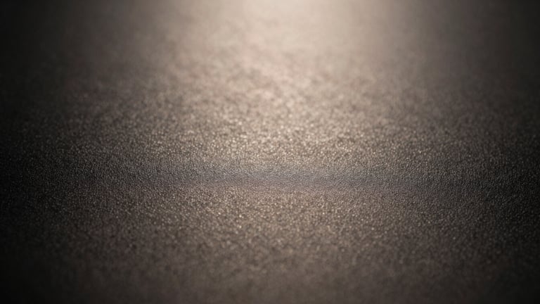 Toma macro de la superficie de una máquina de afeitar mate-negra, mostrando la textura finamente granulada del material. Iluminación lateral dramática, alto contraste, reflejos cálidos y sutiles.