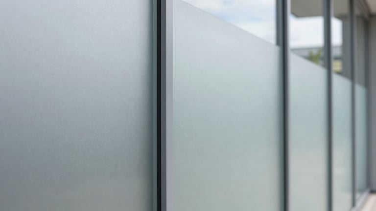 Tight macro shot of the edge of a frosted glass partition, showing the precision cut of the film and its seamless integration with the glass, crisp architectural photography, bright natural daylight, clean glass reflections, cool grey and blue tones, 35mm lens.