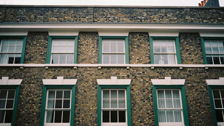 Architectural detail of a classic London brick facade with deep green window frames, soft overcast daylight, desaturated tones, 35mm film
