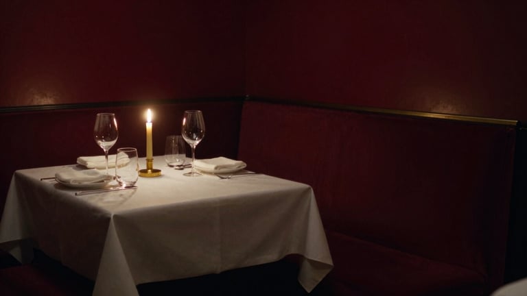 Wide panoramic view of an intimate Parisian dining room at French Savoria, golden candle glow, deep shadows, a single table set to the left third, 35mm