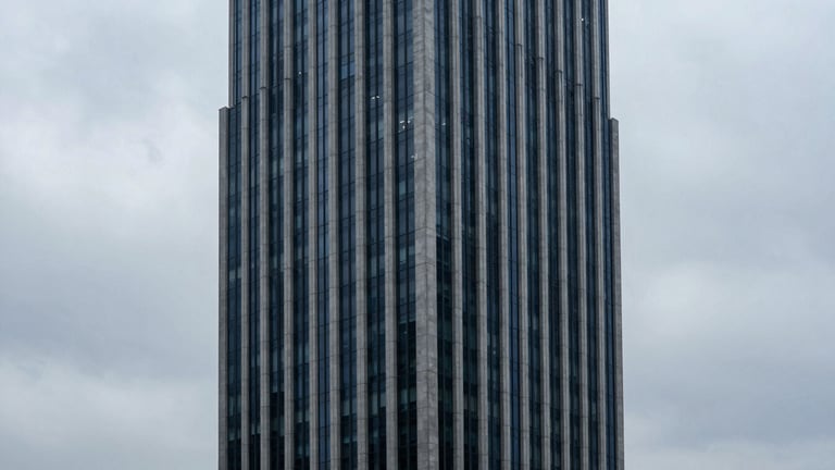 High-angle architectural shot of a financial district skyscraper reaching into cool overcast clouds, sharp clean lines, slate gray and deep navy tones, massive scale.